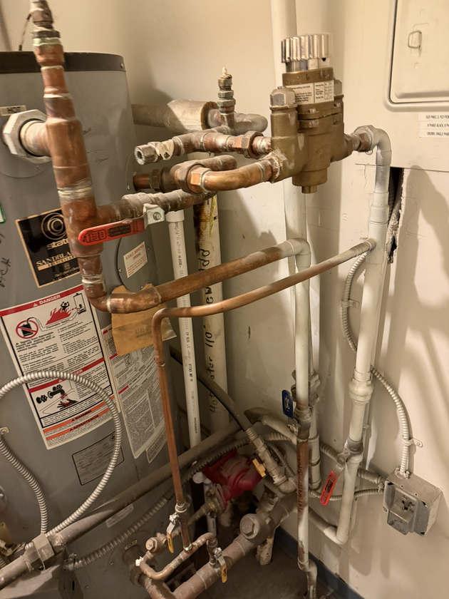 Open wall panel showing plumbing pipes, valves, and a tagged meter