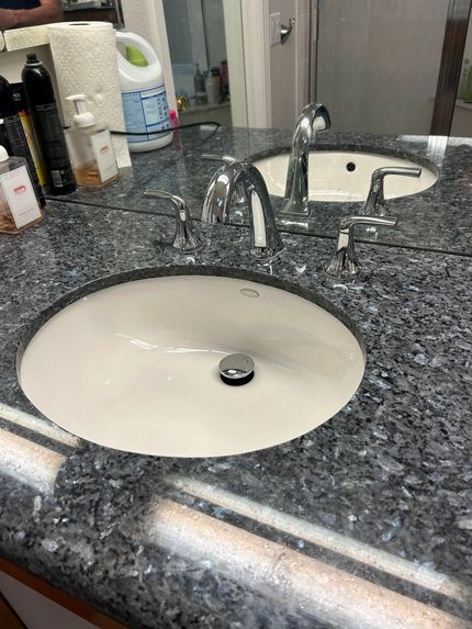 Bathroom sink with granite countertop and chrome faucet beside a toilet tank