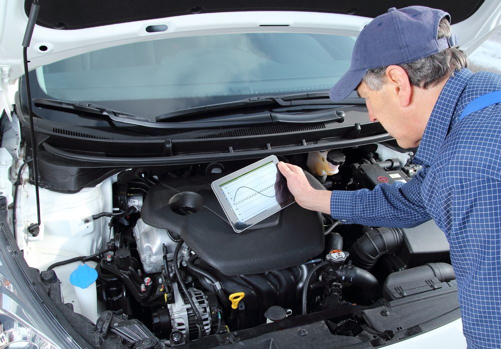 A Man is Working on the Engine of a Car With a Tablet — Port Macquarie Automotive Specialists in Laurieton, NSW