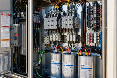 Open electrical control panel with wiring, relays, and capacitors inside a metal cabinet.