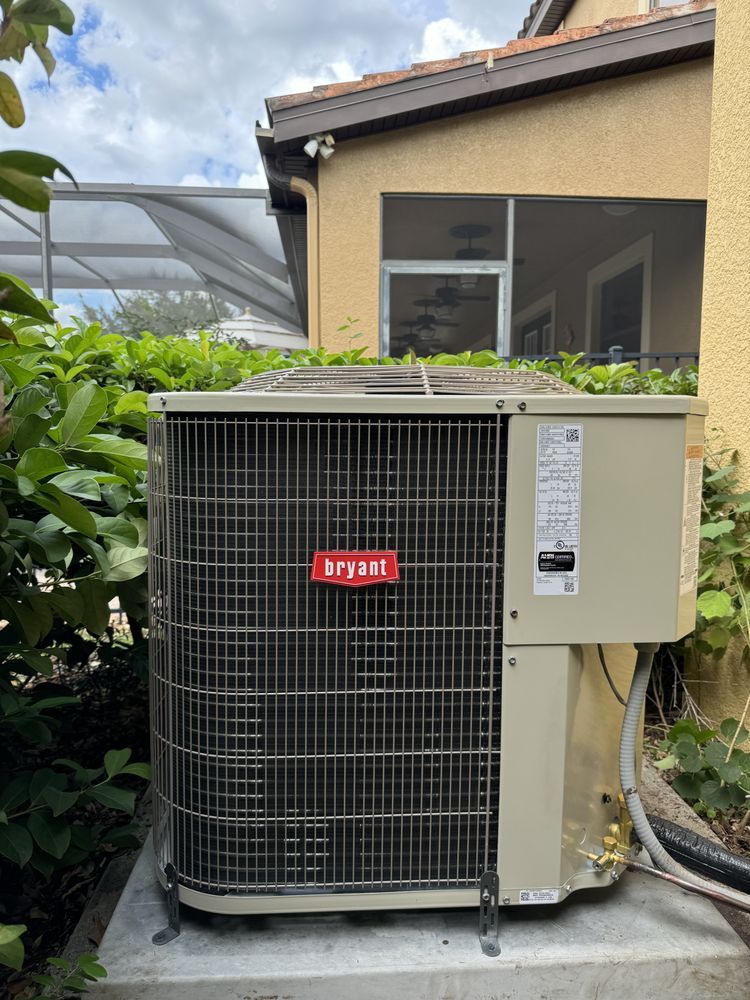Outdoor air conditioner unit beside a house and garden, with a beige wall and window behind it