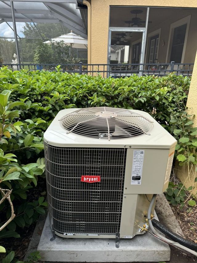 Outdoor air conditioner unit beside green bushes and a building walkway