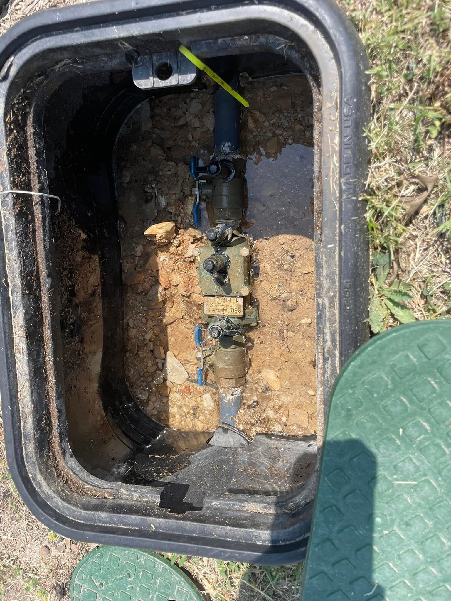 A water meter is sitting in the dirt in a box.