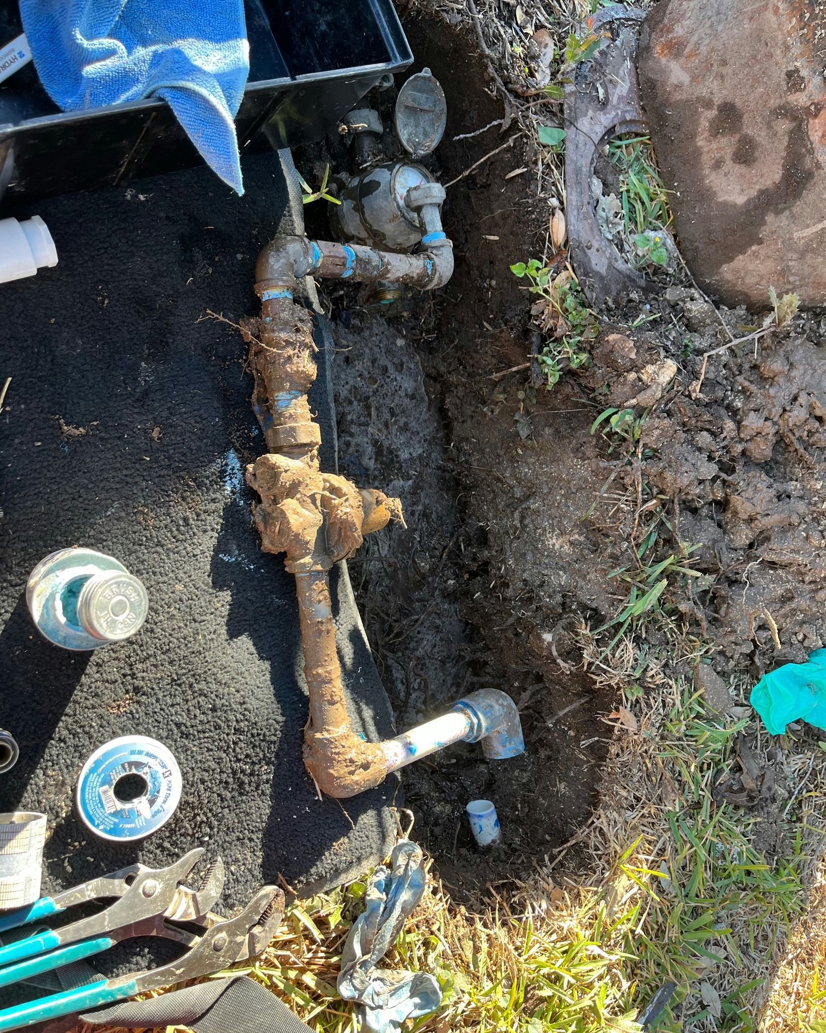 A water meter is sitting in the dirt next to a hose.