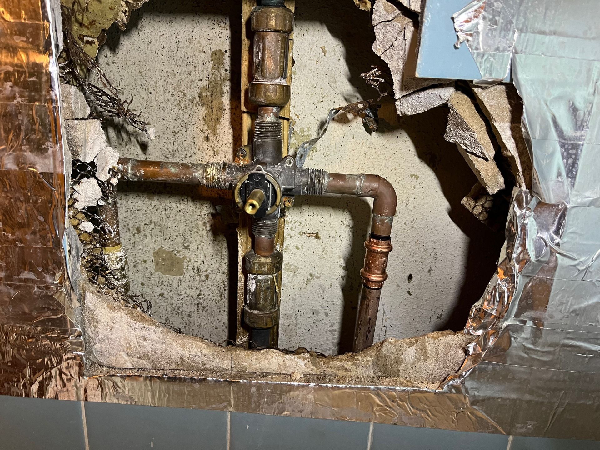 A hole in a wall with copper pipes coming out of it.