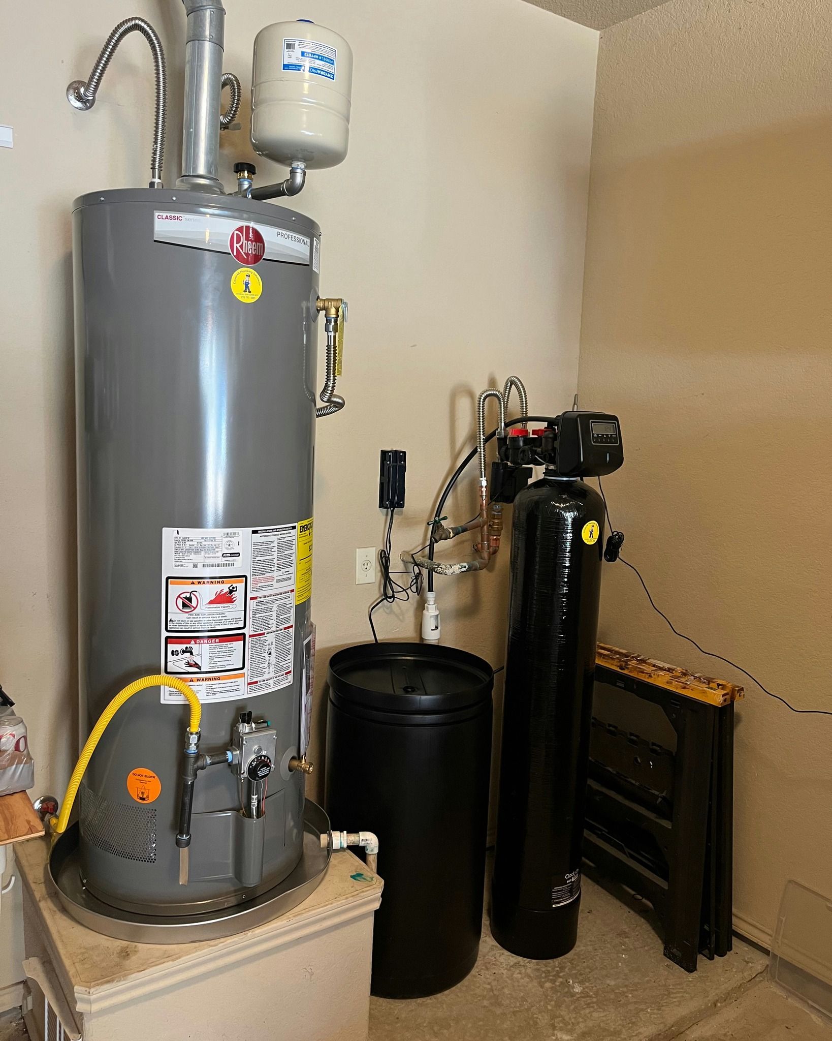 A water heater is sitting in a room next to a black tank.