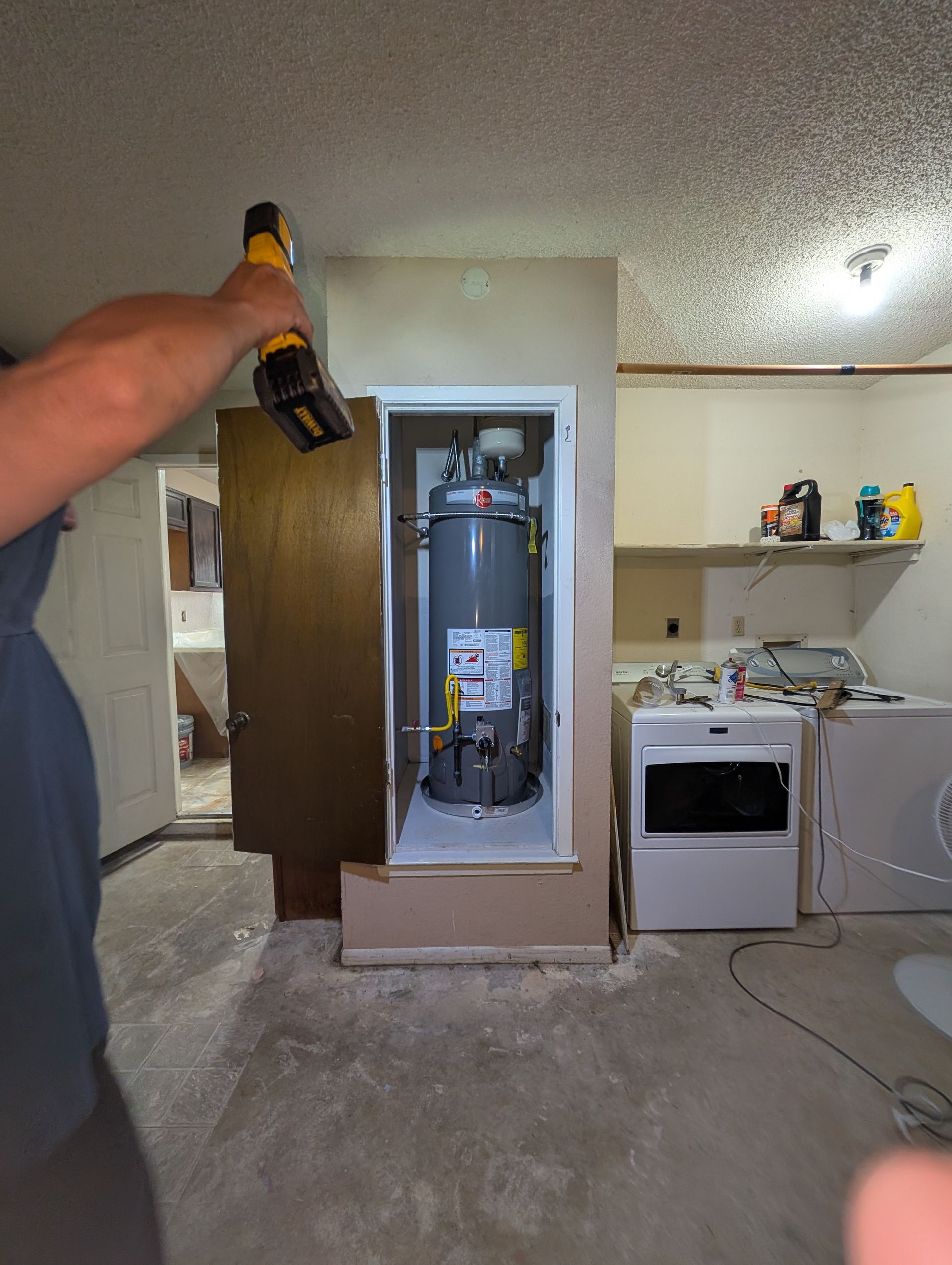 A man is using a drill to install a water heater in a cabinet.