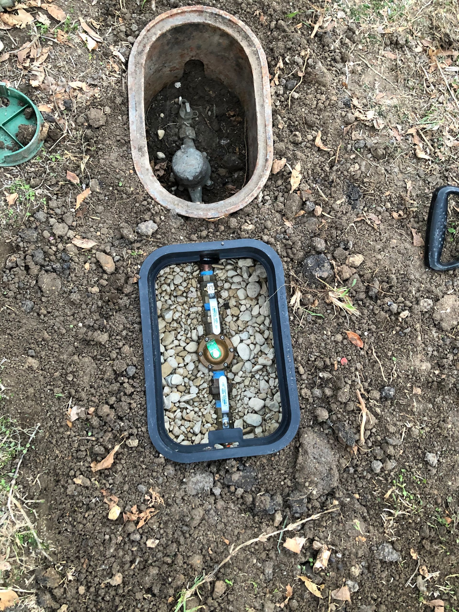 A water meter is sitting in the dirt next to a valve.