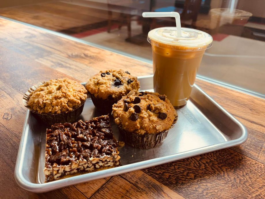 Tray of muffins and a cold coffee drink with a straw on a wooden table.