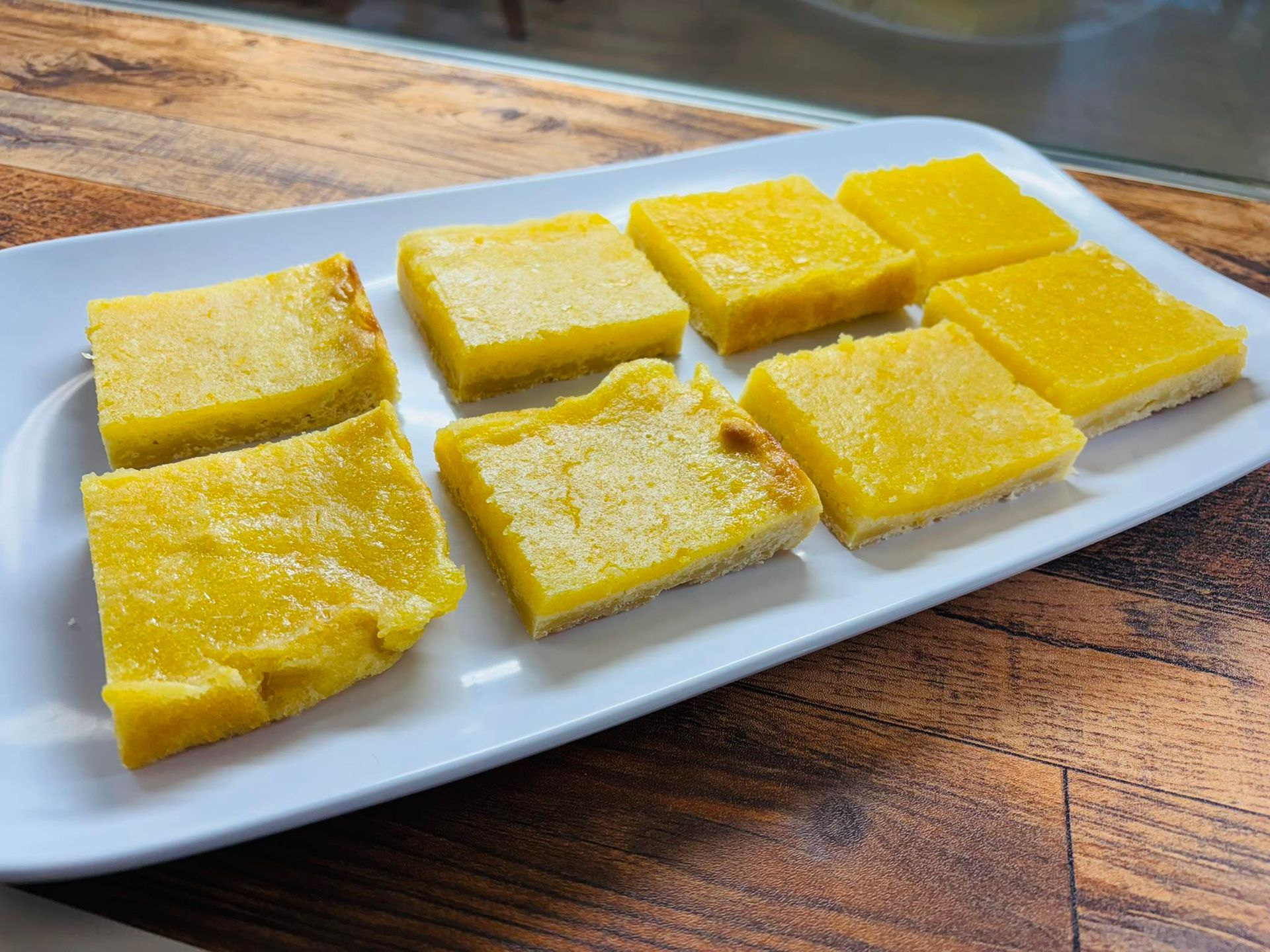 Yellow, square-shaped dessert bars arranged on a white rectangular plate.