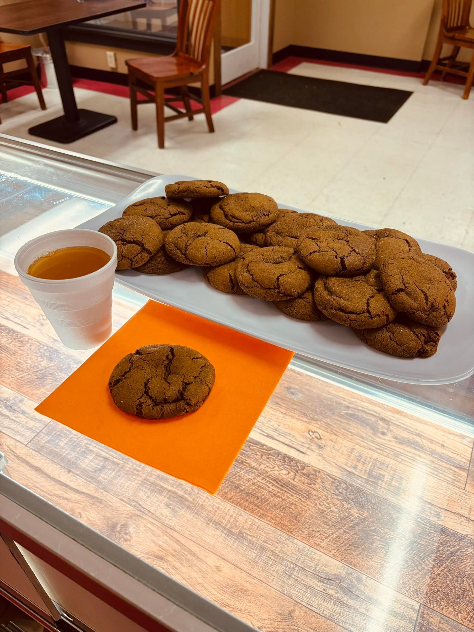 Cookies and tea on a counter. A plate of cookies and one on an orange napkin, with a cup of tea.