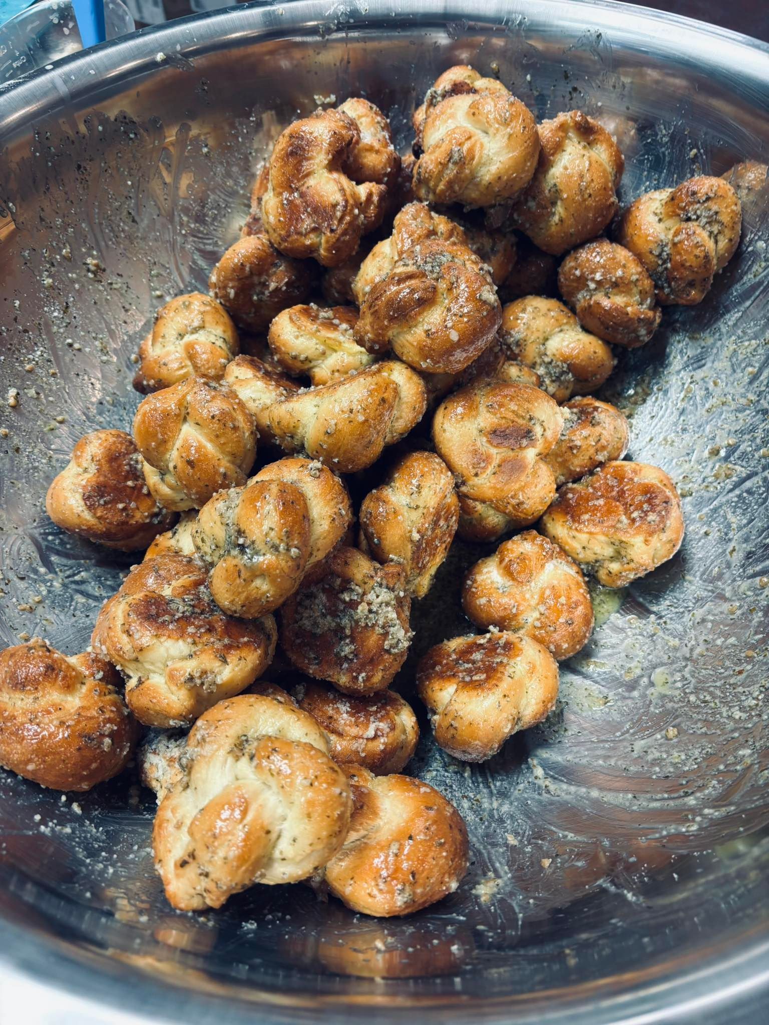 Garlic knots in a metal bowl, seasoned with herbs and spices.