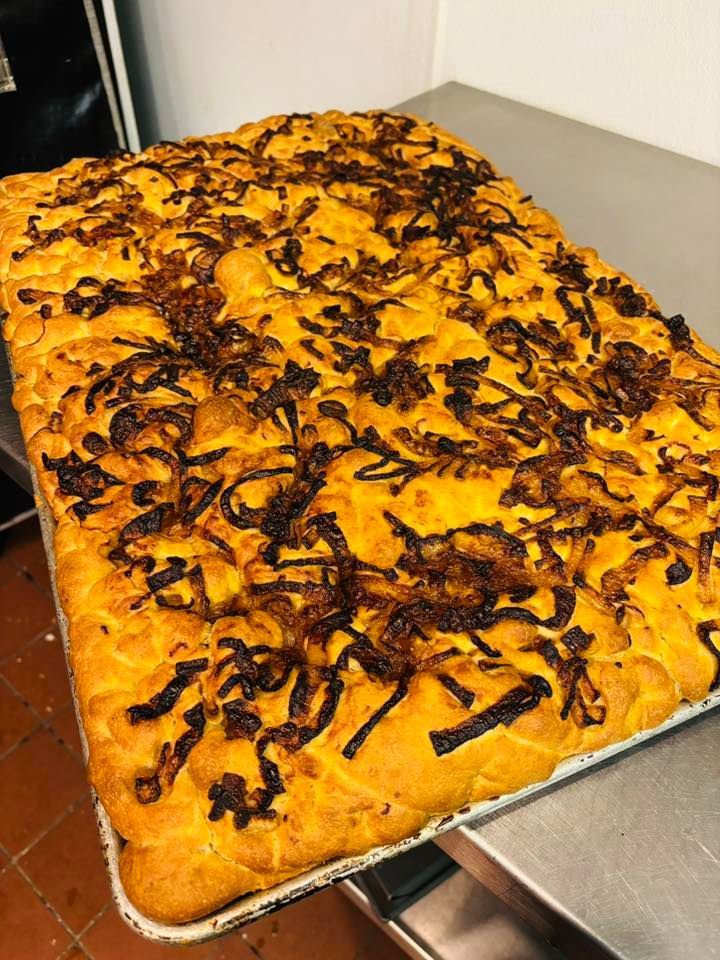 Overhead view of rectangular focaccia bread topped with caramelized onions in a metal pan.