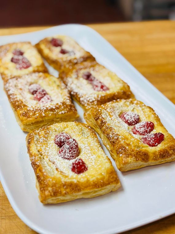 Raspberry pastries dusted with powdered sugar on a white rectangular plate, on a wooden surface.