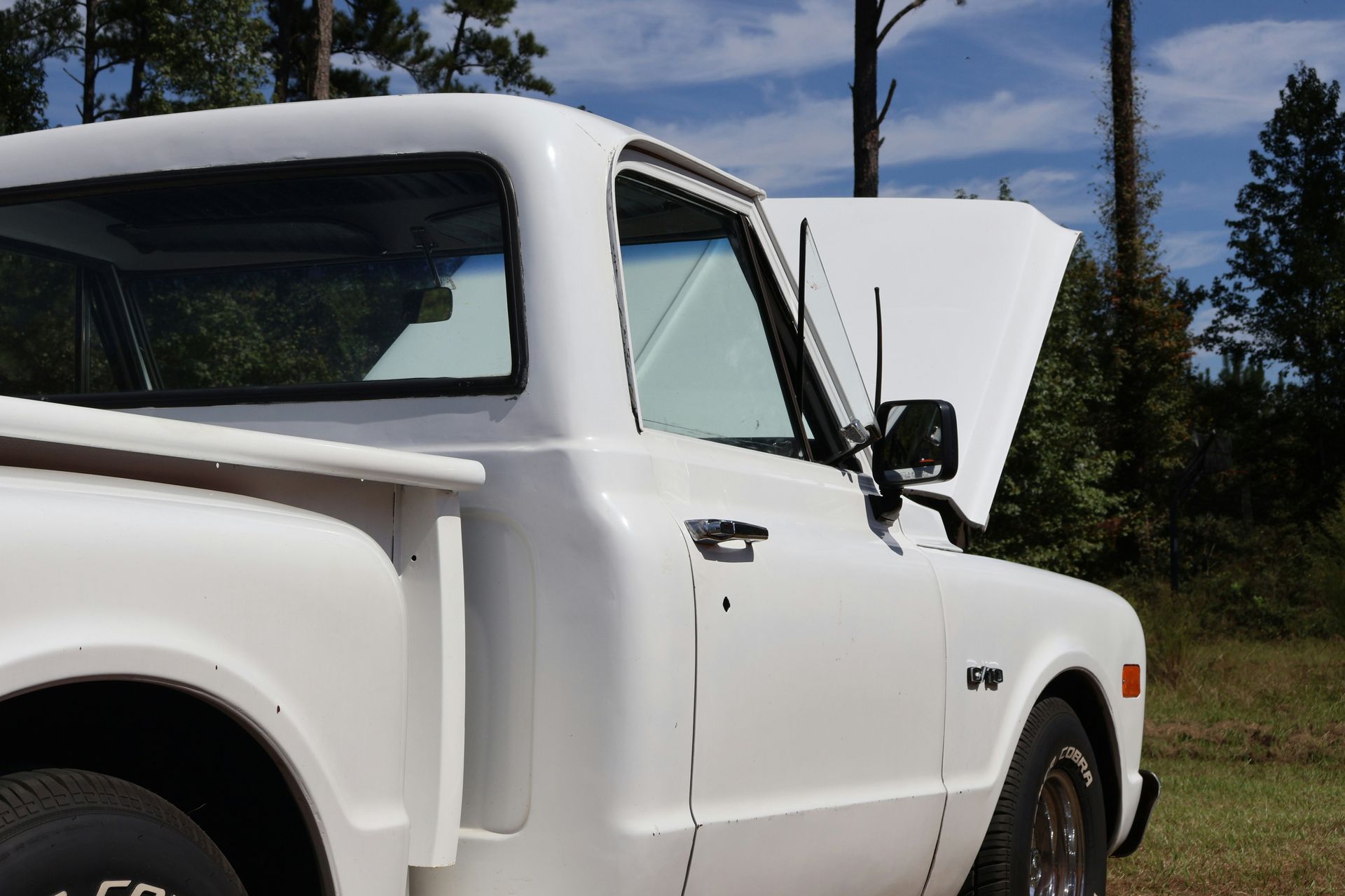 A white truck with the hood up is parked in a field