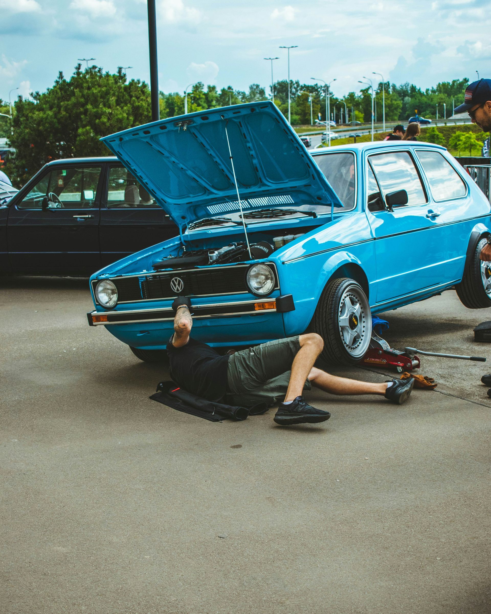 A man is laying on the ground working on a blue car.