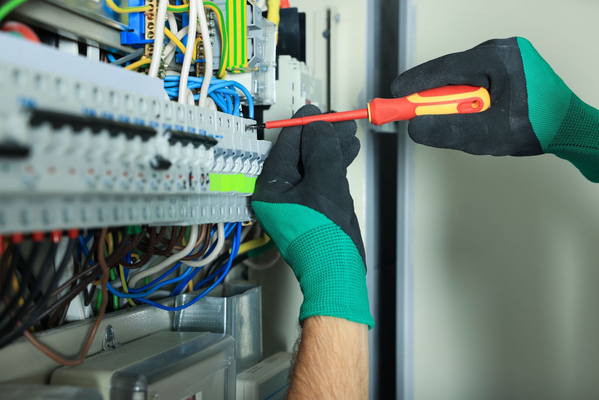 Electrician tightening wires in a circuit breaker panel, wearing gloves.