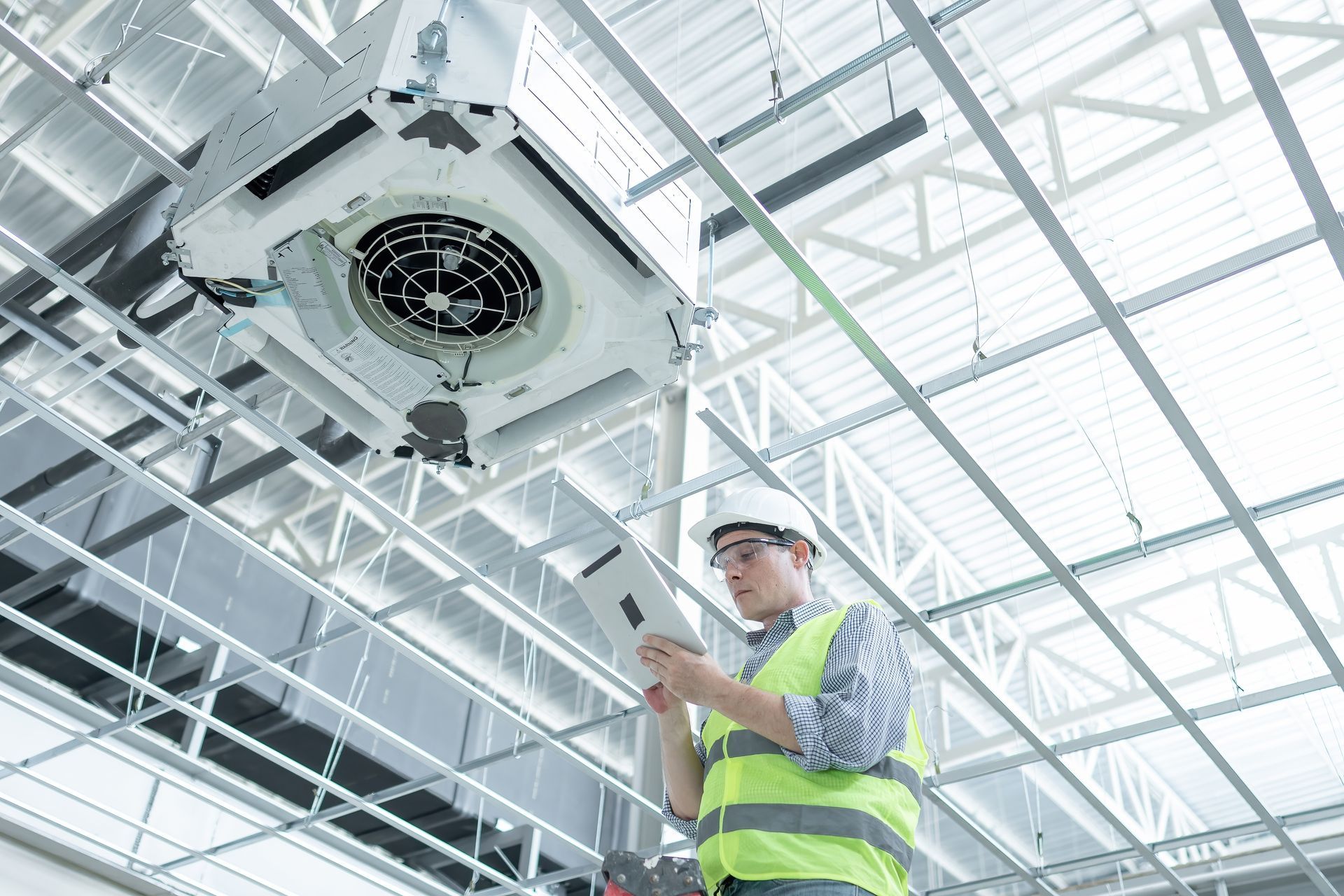 HVAC technician inspecting ceiling-mounted air conditioning unit in a large building.