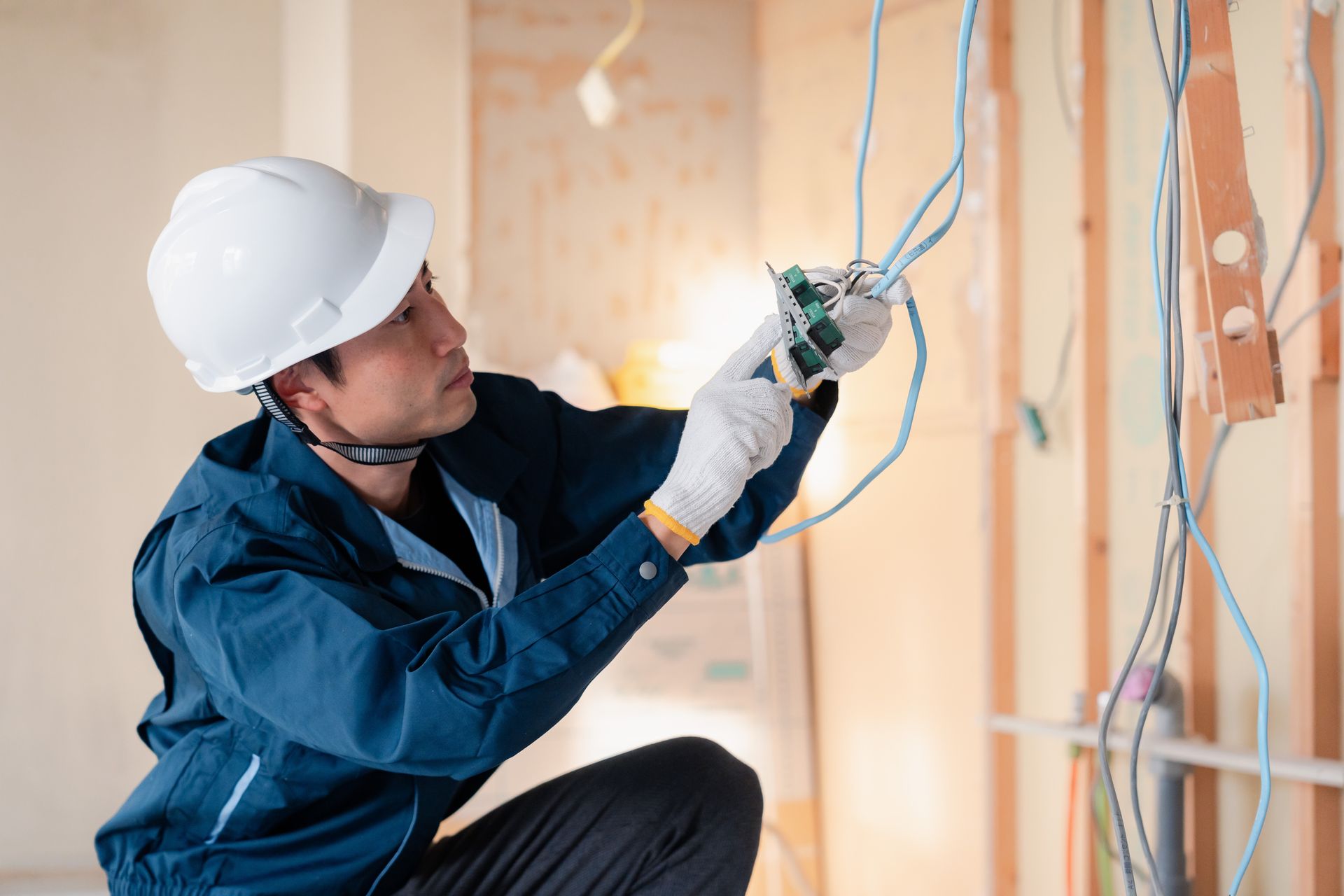 Electrician in white hard hat, connecting wires to an electrical outlet during construction.