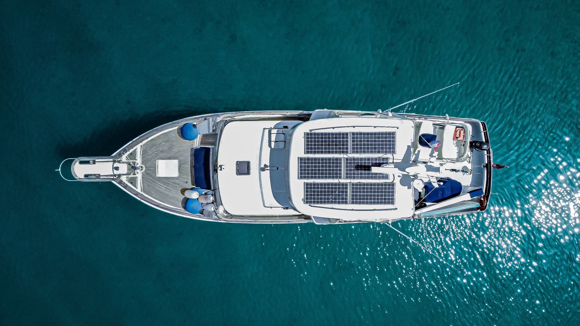 Overhead view of a white yacht with solar panels on a turquoise sea.