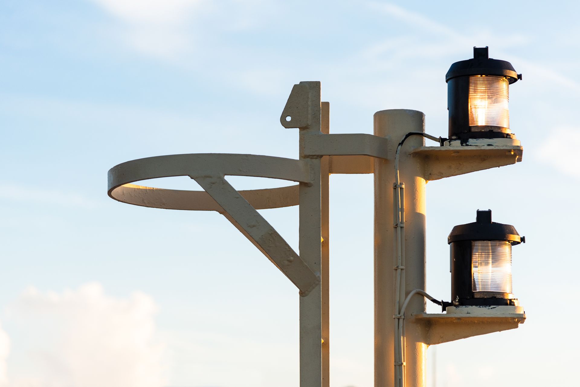 Metal pole with two nautical lights, a circular ring, against a blue and yellow sky.