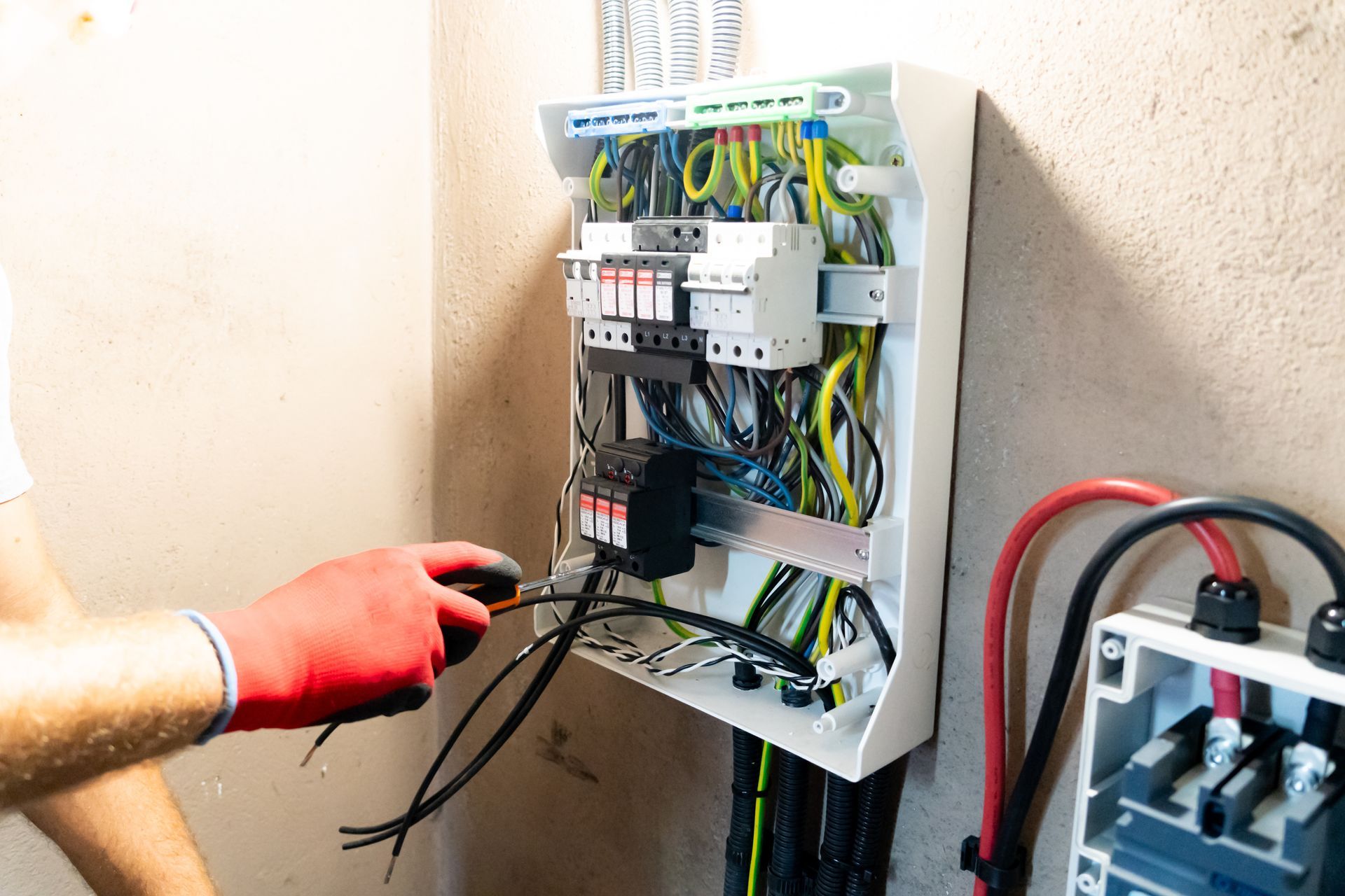 Person in red gloves working on electrical panel with wires and circuit breakers.