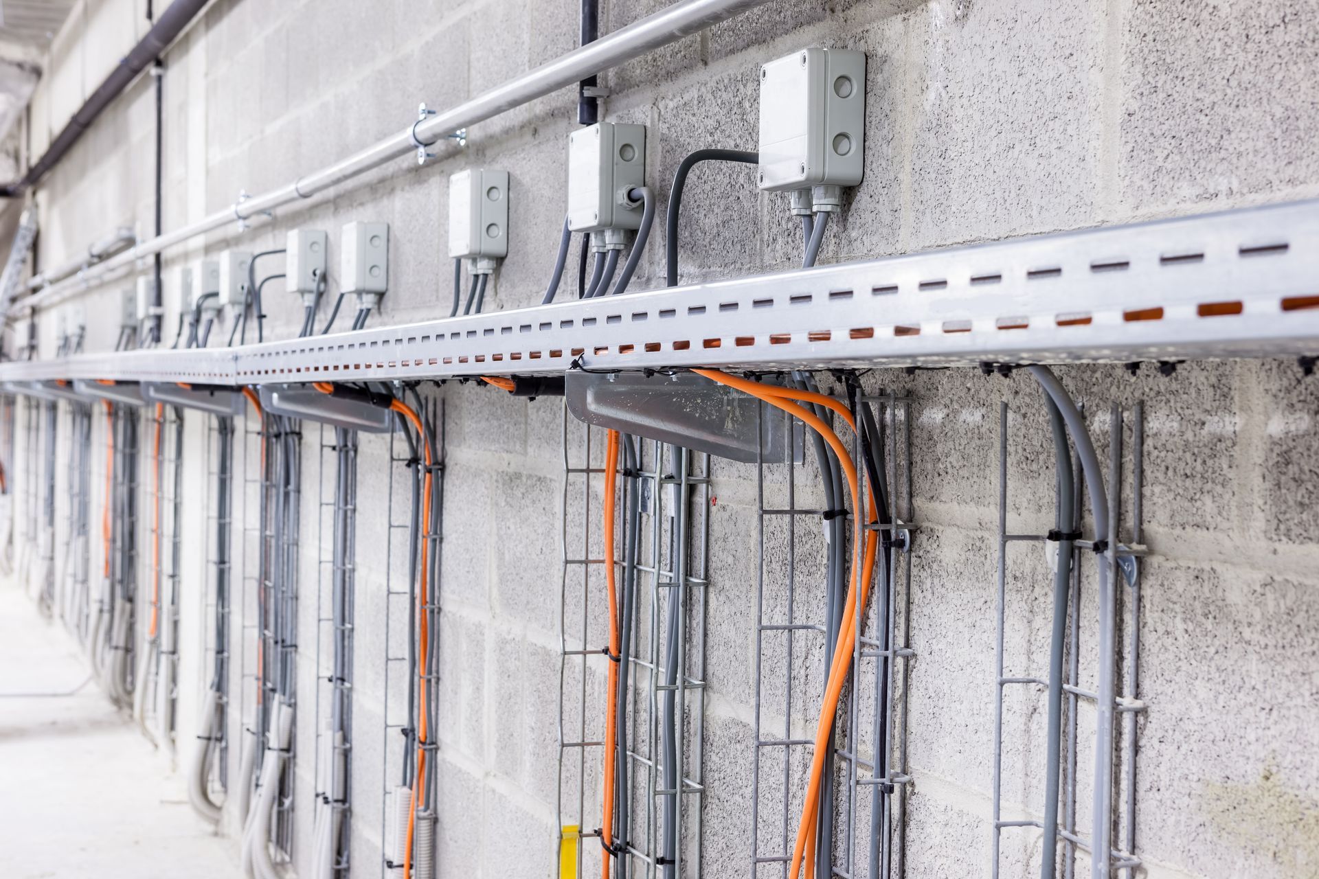 Gray electrical conduit and cable trays along a cinder block wall, with several junction boxes.