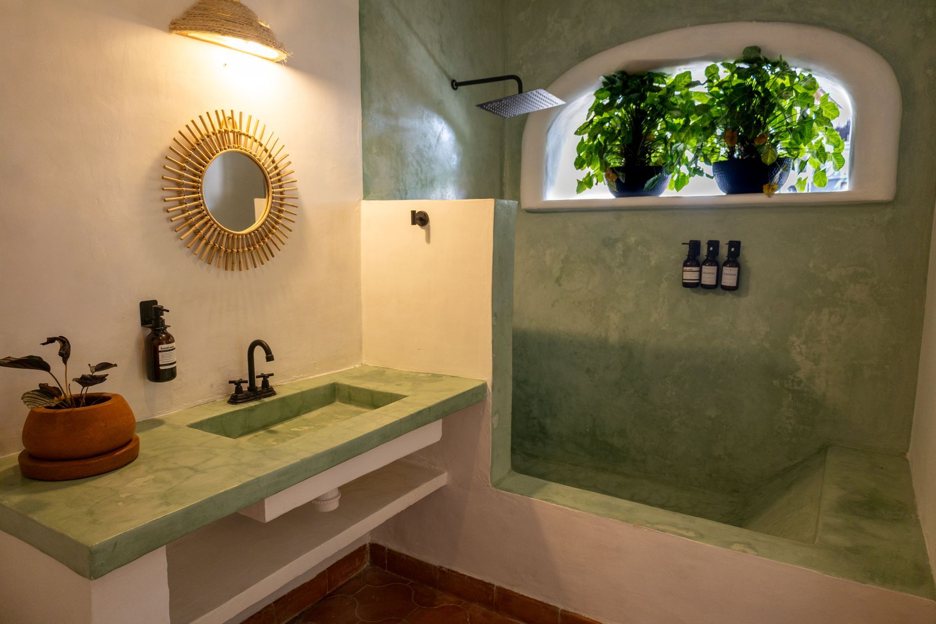 Baño con paredes texturizadas verdes, lavabo, ducha, ventana con plantas.