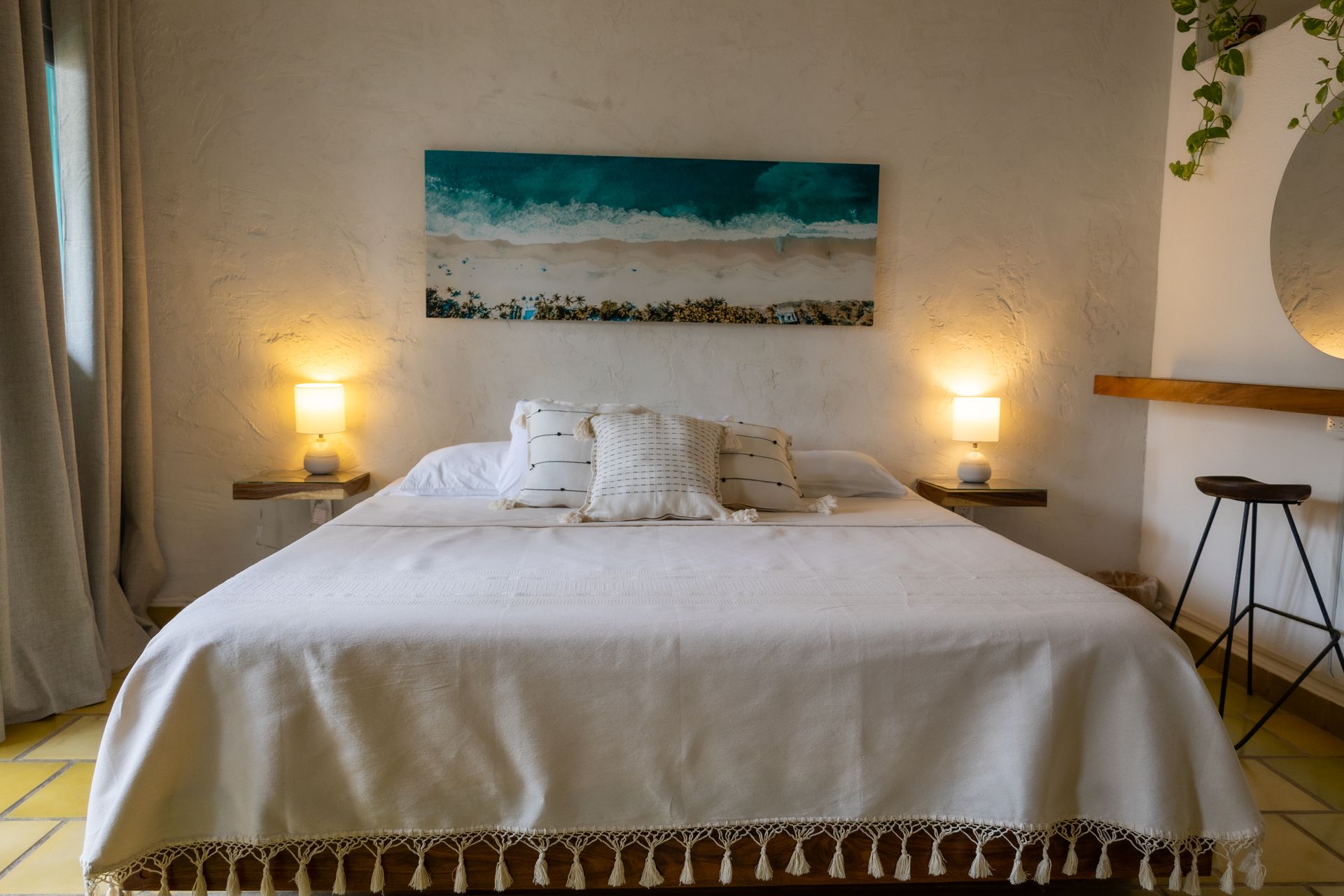 Dormitorio con ropa de cama blanca, arte turquesa y dos lámparas de noche.