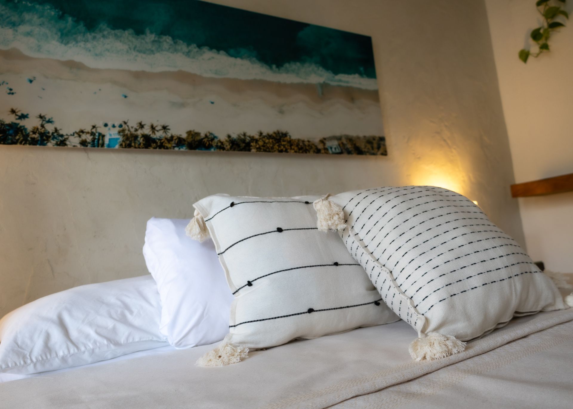 Cama con sábanas blancas, almohadas decorativas y un cuadro con temática de playa encima.
