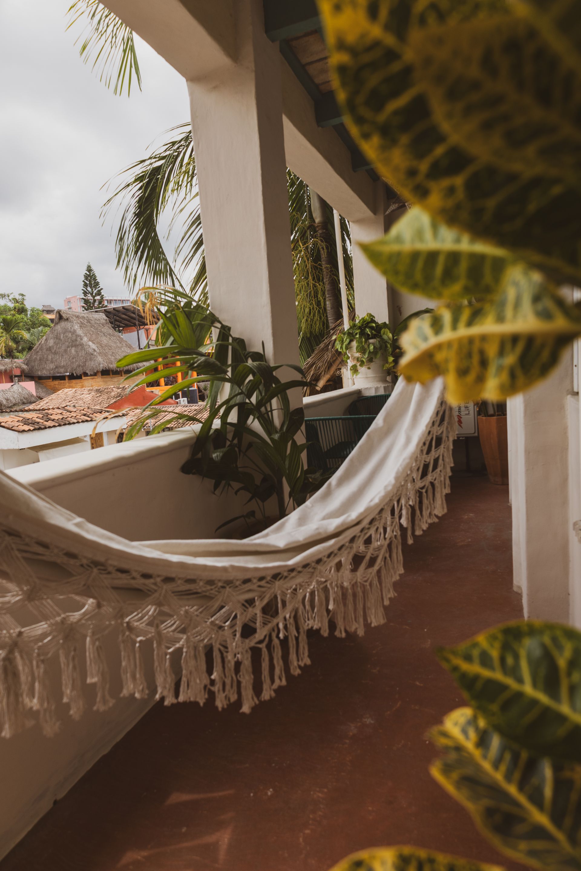 Hamaca blanca en un balcón con plantas, con vista a edificios con tejados rojos.