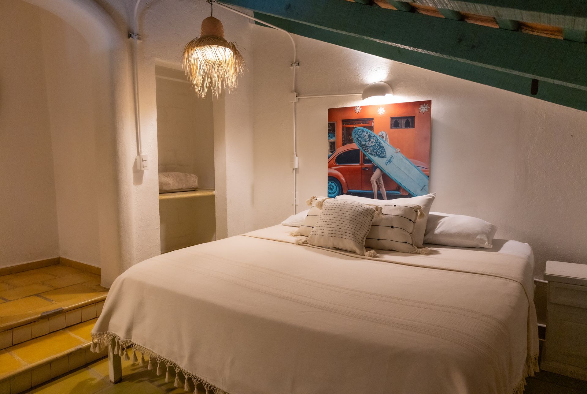 Dormitorio con cama, obra de arte de un coche de surf, estanterías y una luz decorativa.