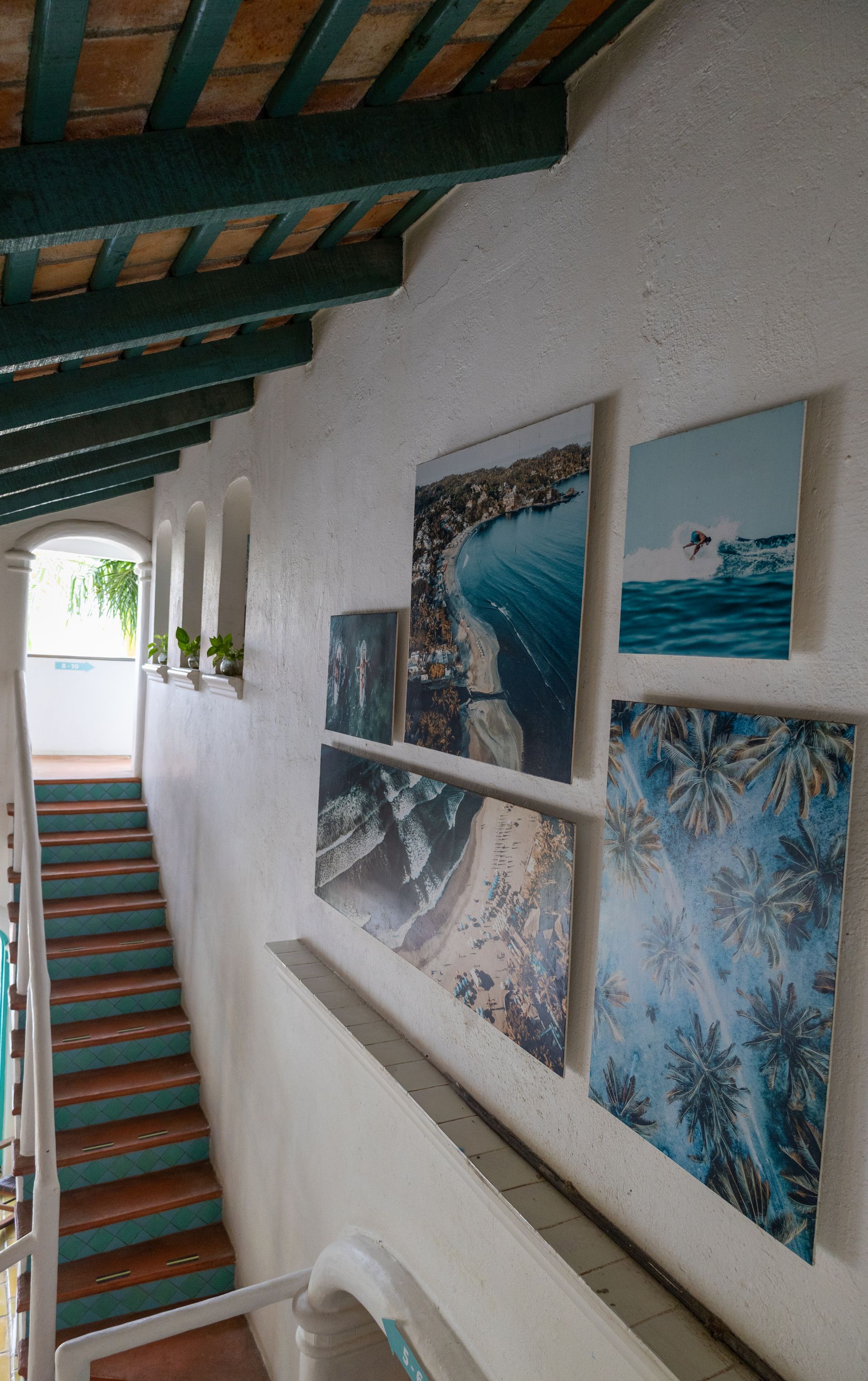 Escalera con paredes blancas, pinturas de vistas al mar y techo verde.