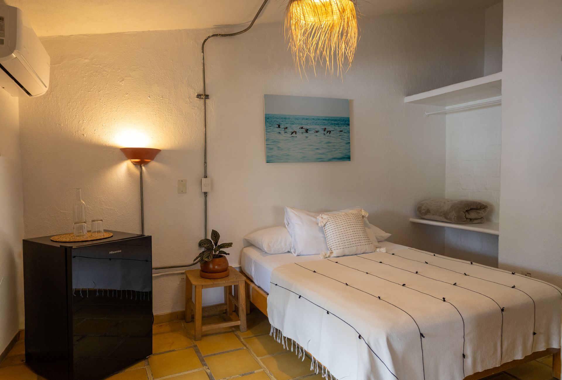 Dormitorio pequeño y luminoso con cama individual, pequeño armario, lámpara y aire acondicionado.