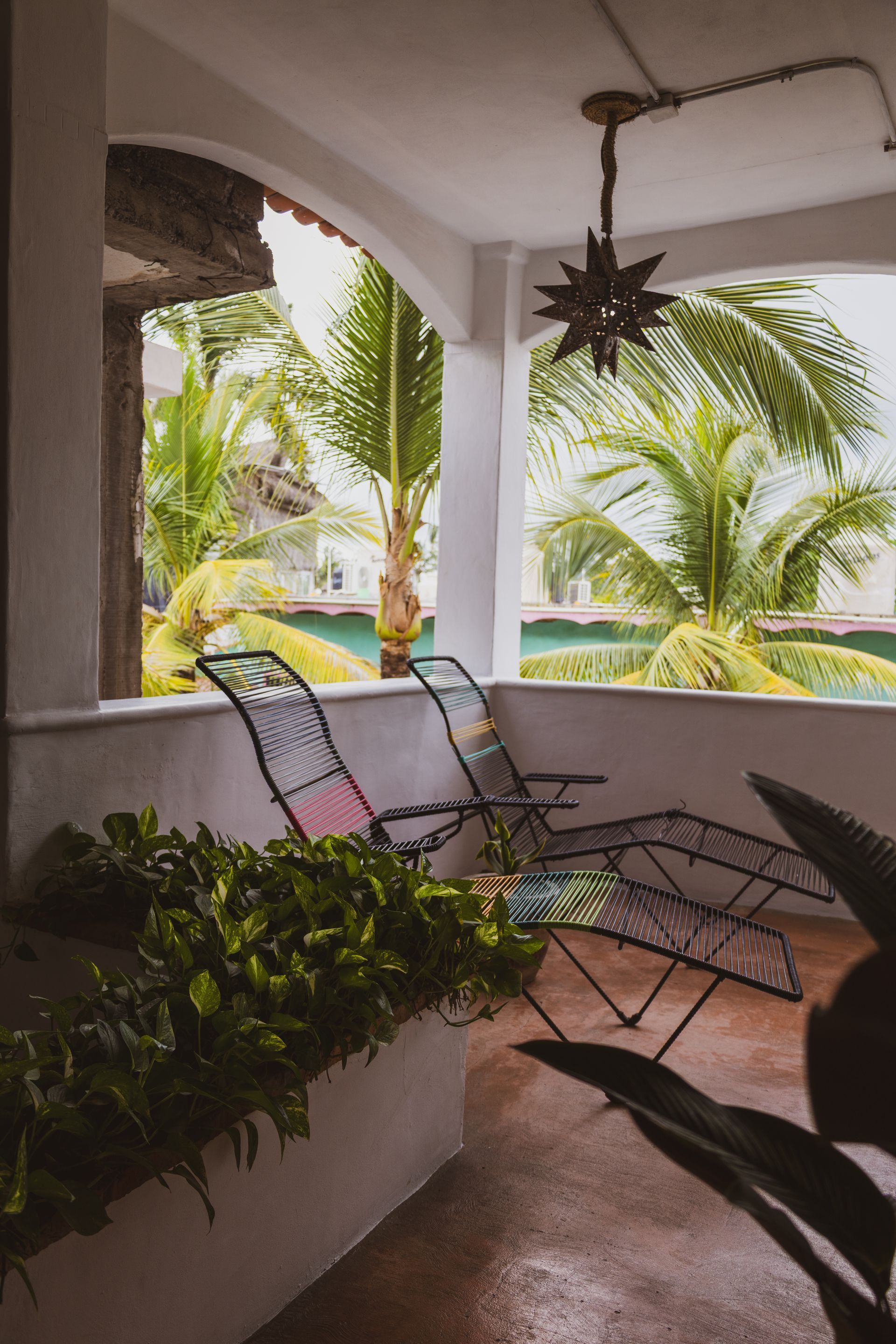 Patio con dos sillas de metal, vegetación, palmeras y lámpara en forma de estrella.