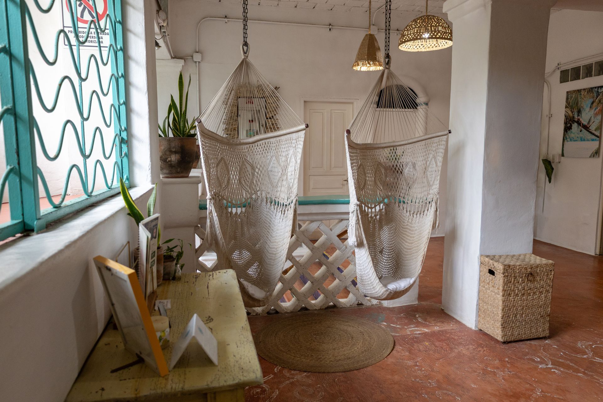 Dos sillas colgantes de macramé en una habitación con una mesa de madera, una alfombra redonda y una ventana.