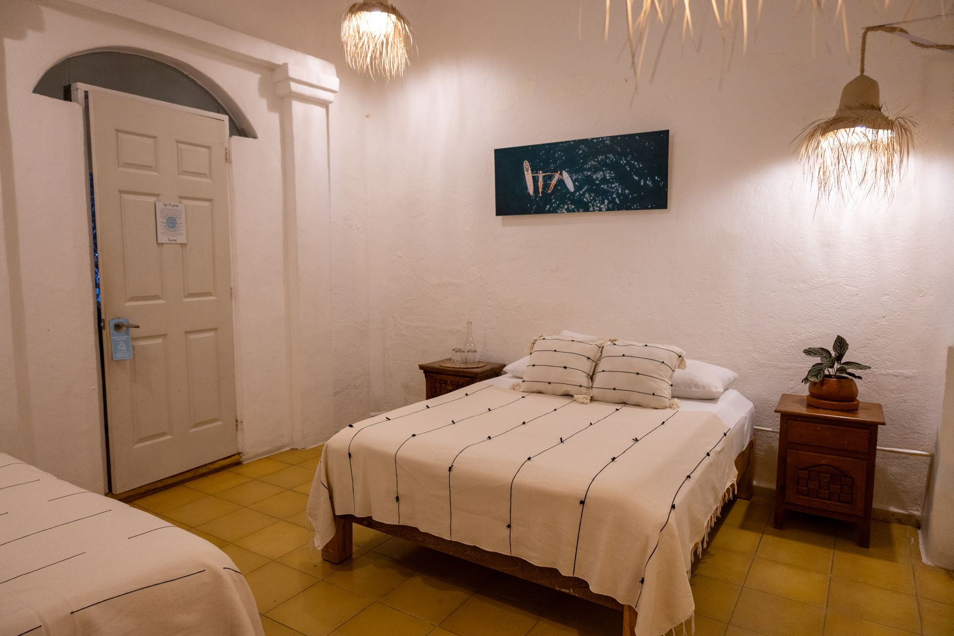 Dormitorio con dos camas, paredes blancas, iluminación decorativa y puerta.