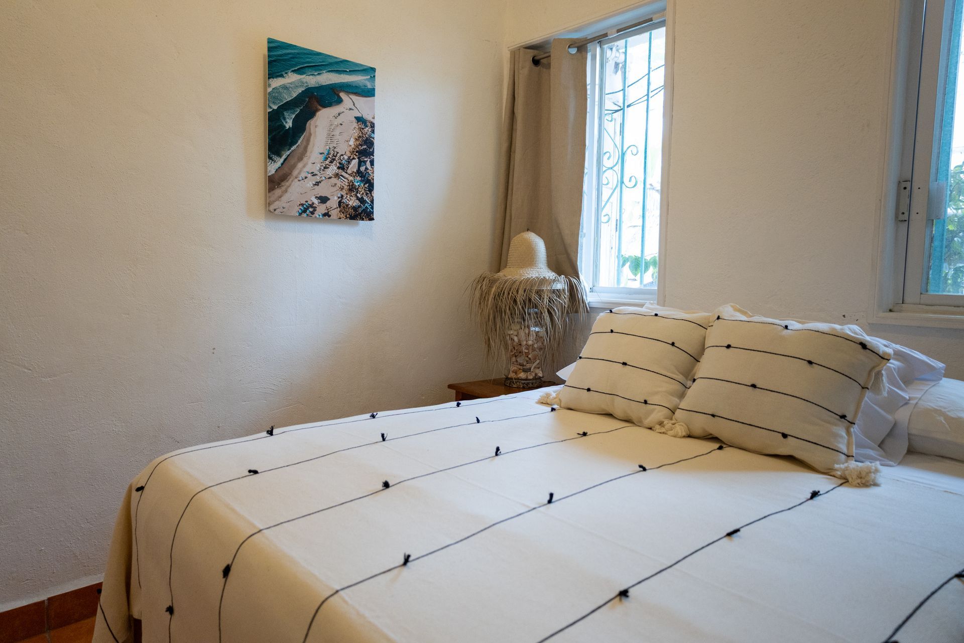 Dormitorio con cama blanca, obras de arte costeras y ventana con cortina.