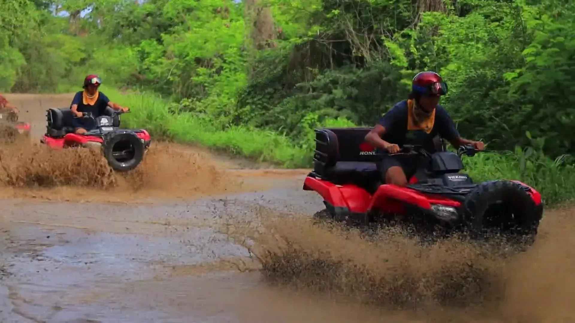 Conductores de vehículos todo terreno chapoteando en el barro en un camino de tierra, con árboles en el fondo.