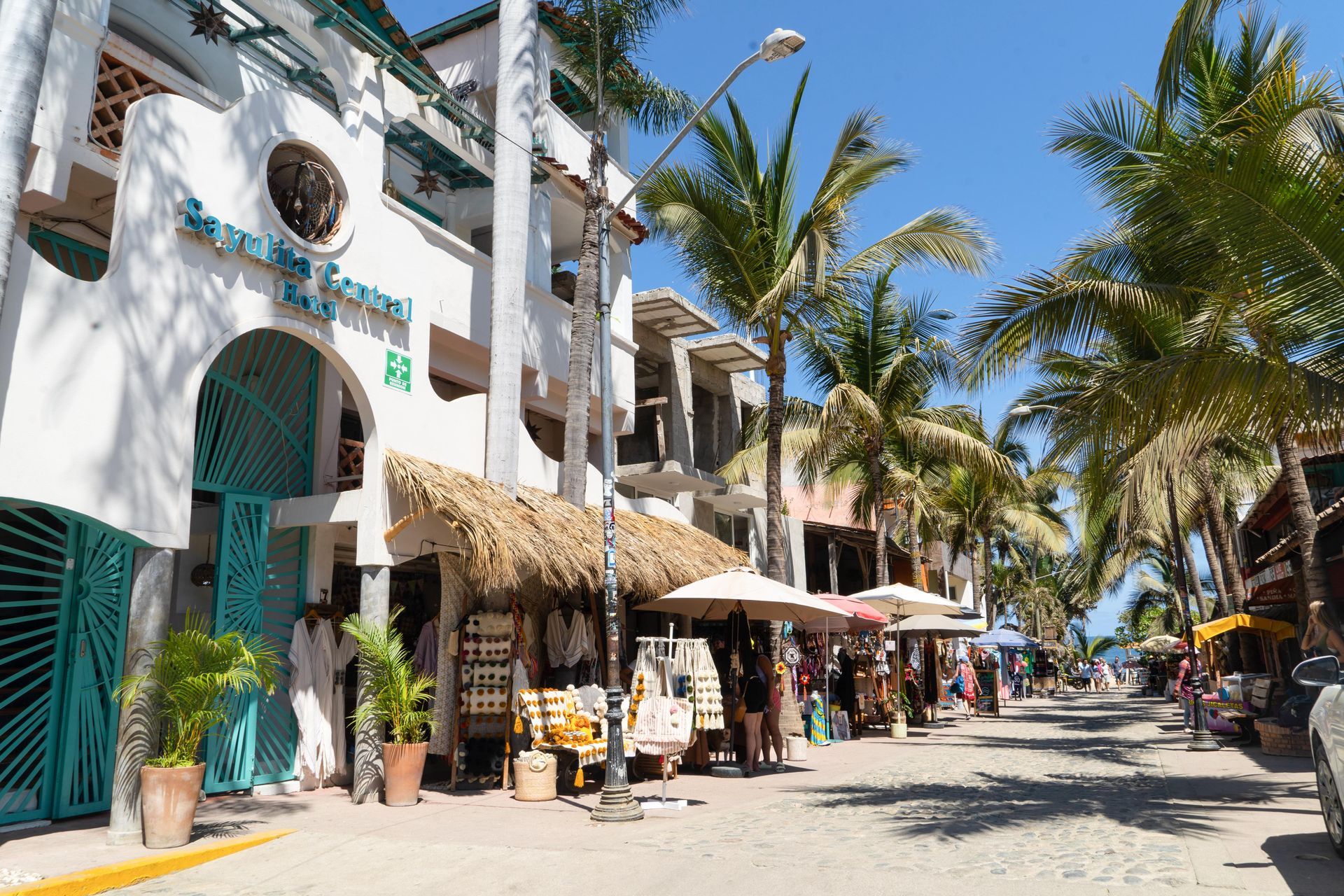 Escena callejera en Puerto Vallarta con tiendas, palmeras y cielo azul.