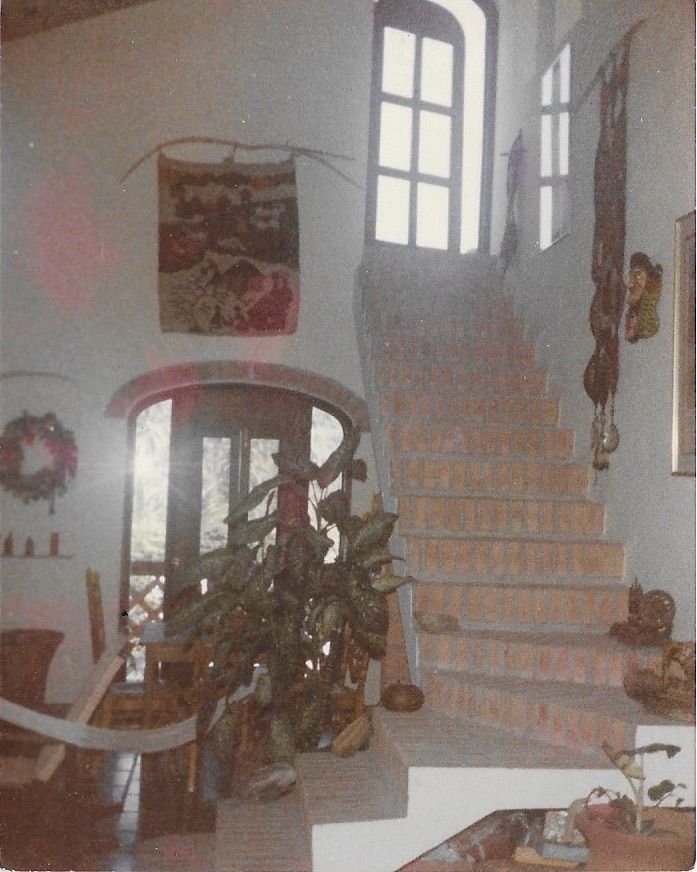 Una escalera conduce a una casa. Se ve una puerta, una planta y adornos en las paredes.