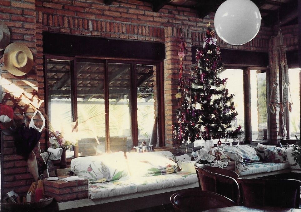 Interior con un árbol de Navidad cerca de una ventana, con una pared de ladrillos y una luz de globo blanca colgando.