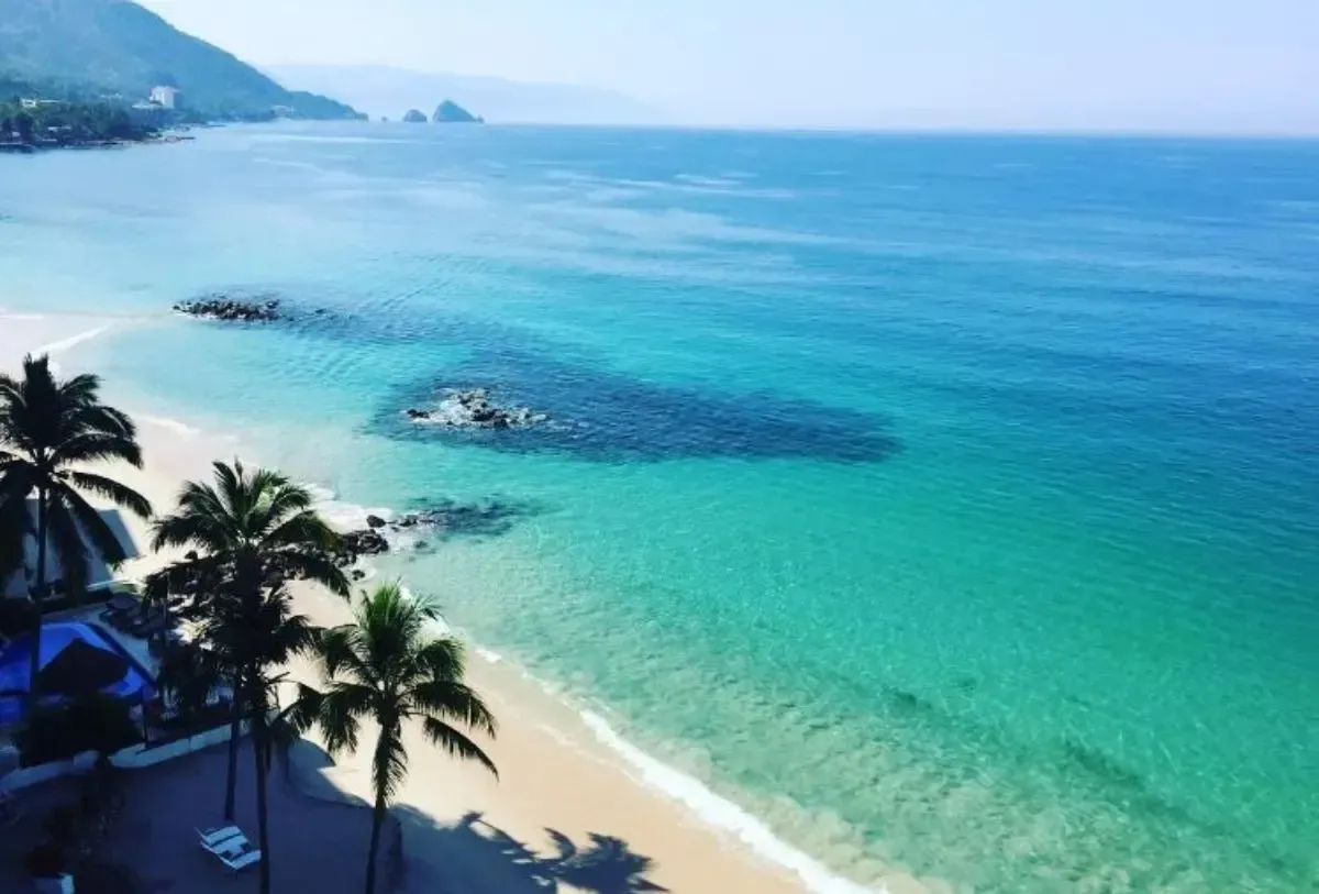 El océano turquesa se encuentra con una playa de arena blanca con palmeras. Día soleado y despejado.