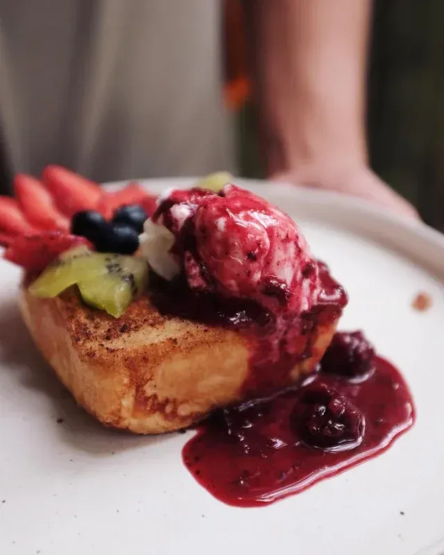 Tostada francesa cubierta con frutas, bayas y salsa en un plato blanco.