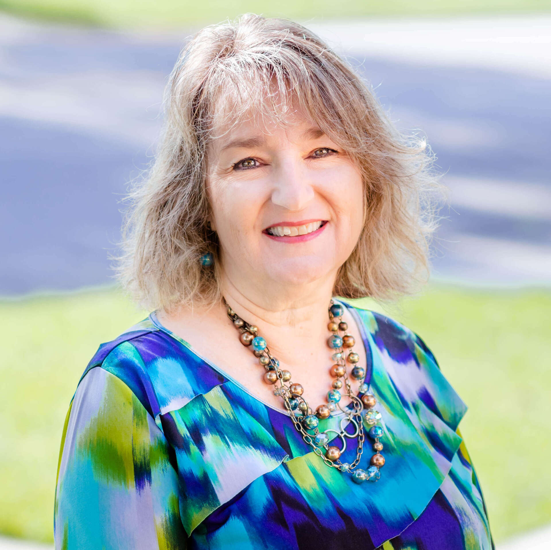 A woman wearing a blue shirt and a necklace smiles for the camera