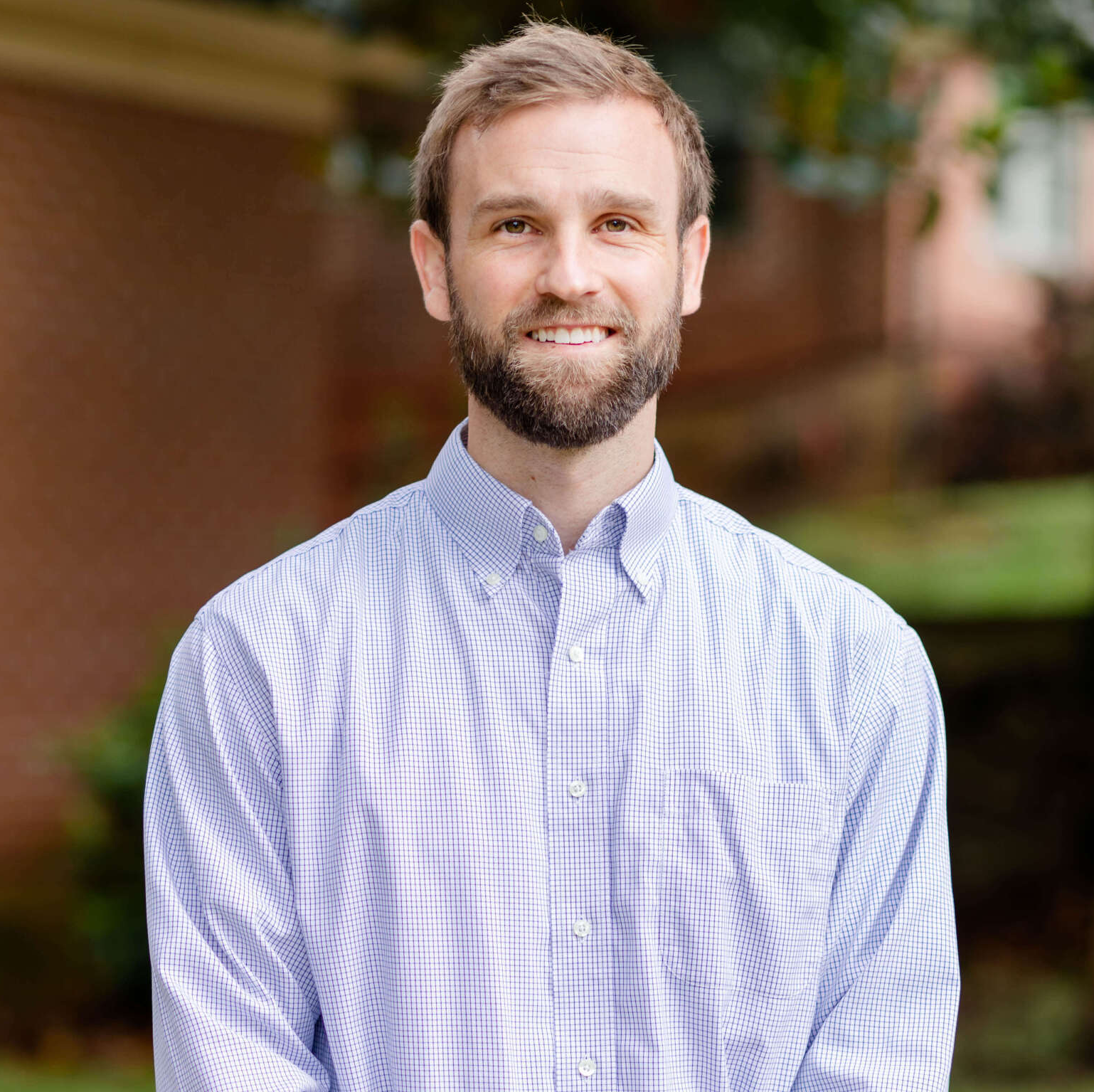 A man with a beard is wearing a plaid shirt and smiling