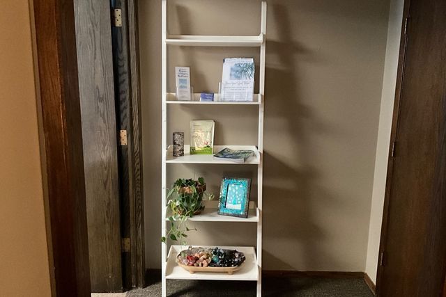 A white ladder shelf is sitting in a hallway next to a door.