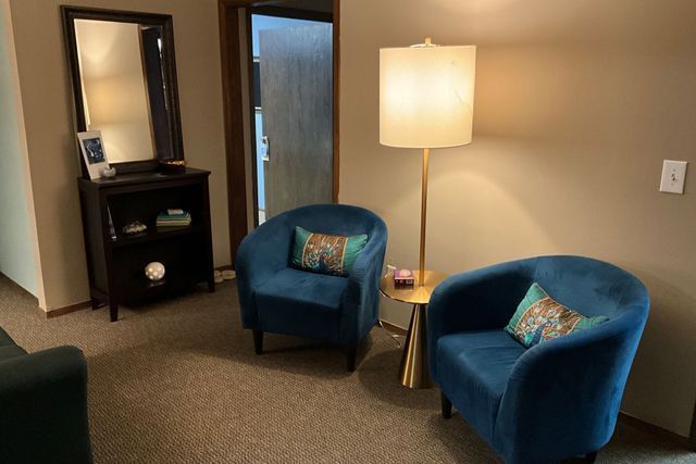 A waiting room with two blue chairs and a lamp.
