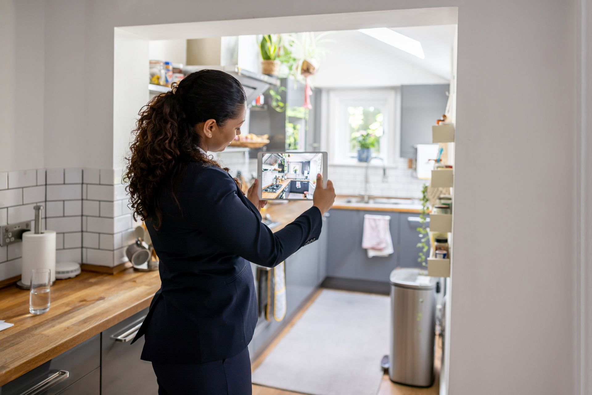 A woman is taking a picture of a kitchen with a tablet.