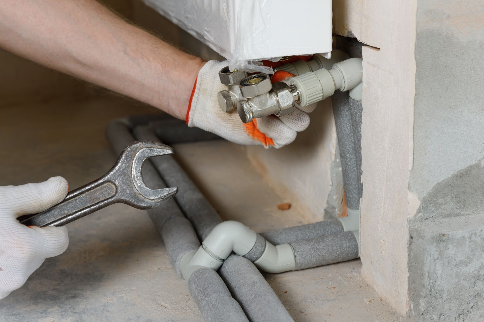 A plumber is attaching the pipes of the heating system to the radiator. A plumber is attaching the pipes of the heating system to the radiator.